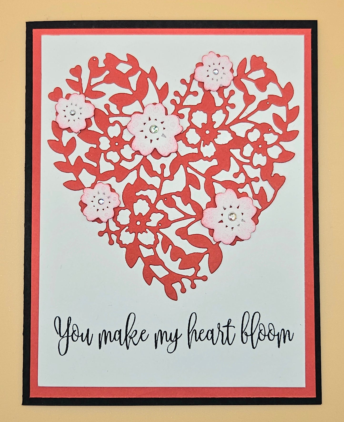 Framed artwork with a floral heart design and text 'You make my heart bloom' on a beige background.