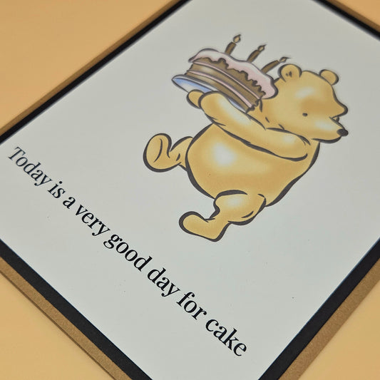 Handmade Winnie the Pooh birthday card with Pooh carrying a birthday cake with lit candles on white inner panel with black and tan border. Text reads Today is a very good day for cake.