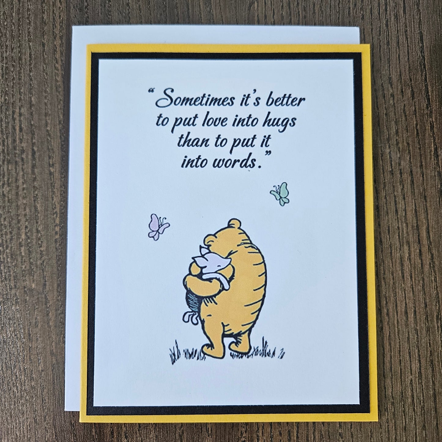 Card with Winnie the Pooh hugging a bear and a quote about love and hugs on a beige background.