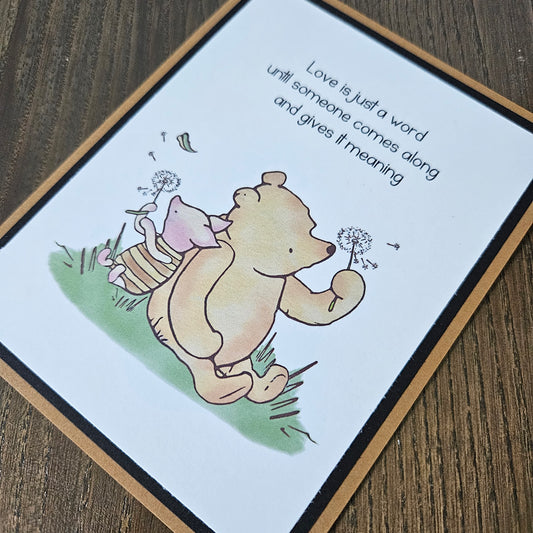 Card with cartoon bear and piglet blowing dandelion seeds on a wooden surface