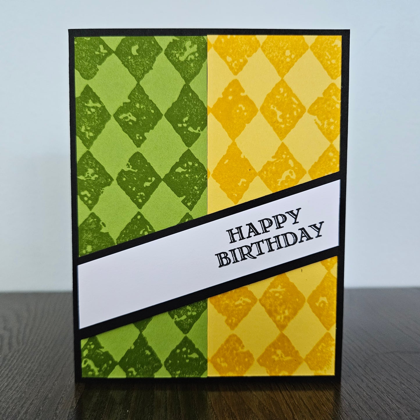 Handmade birthday card for him with green and yellow argyle stamped panels and diagonal banner on black border. Text reads Happy Birthday.