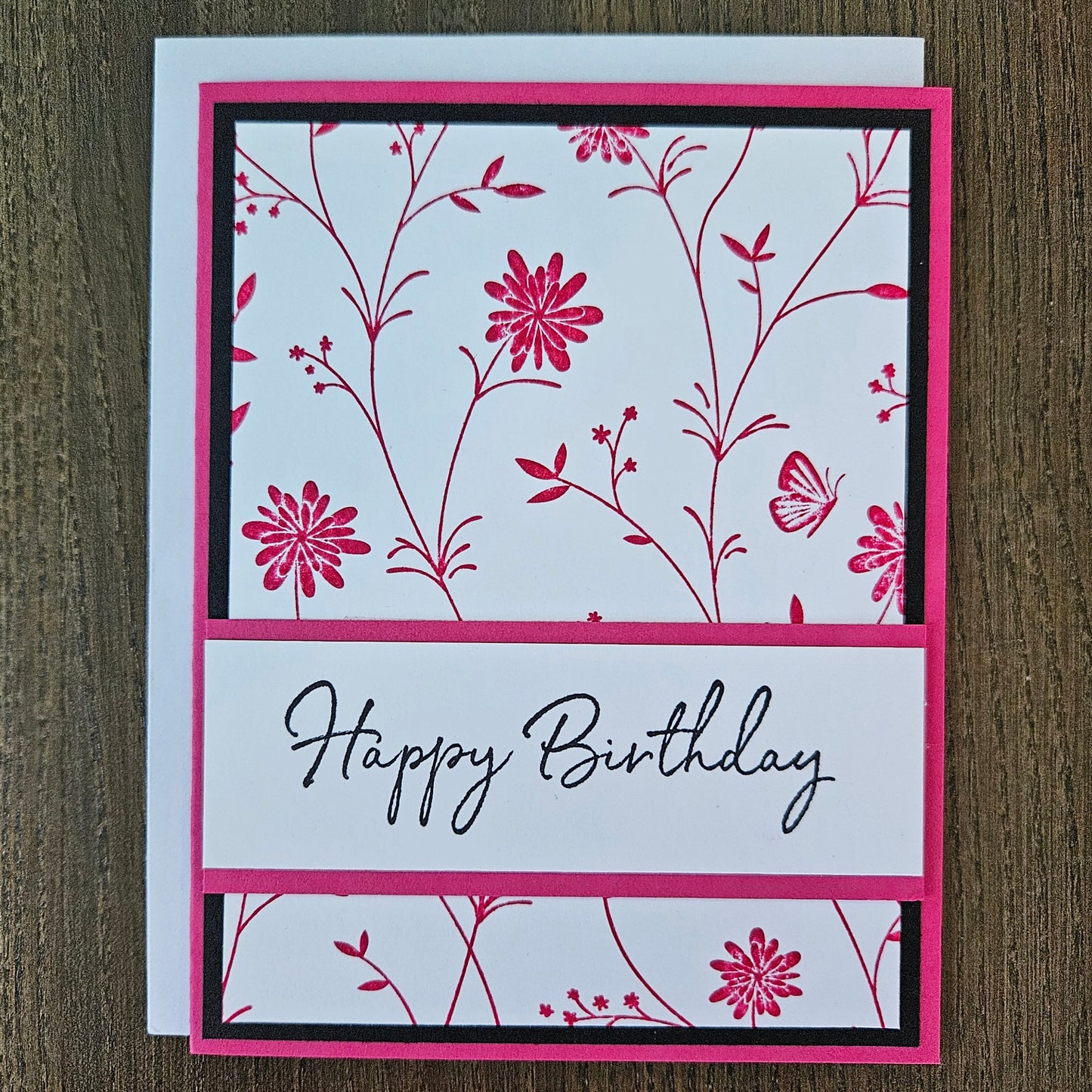 Handmade birthday card for her with pink hand-stamped wildflowers and butterfly design with split banner on black and pink border. Text reads Happy Birthday.