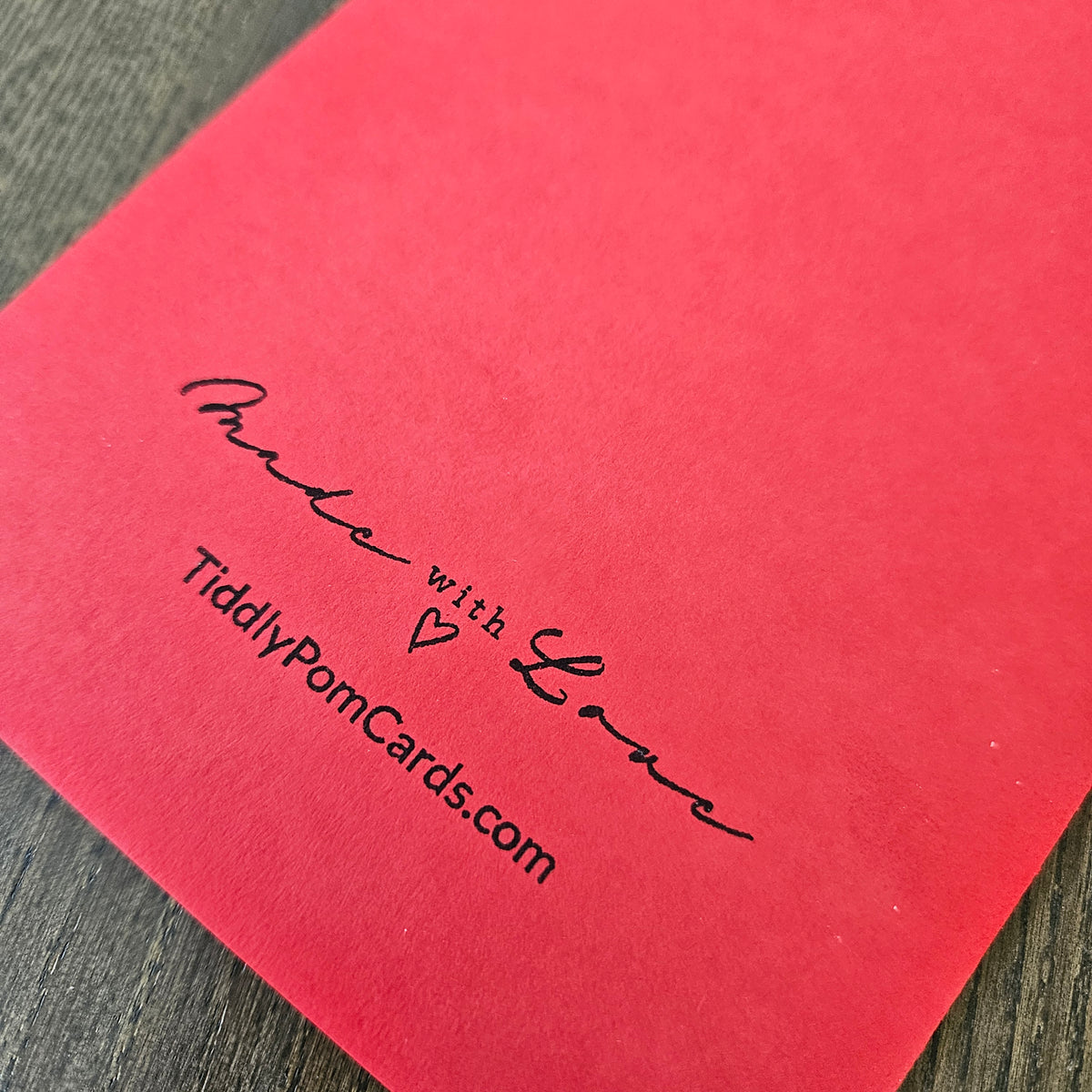 Red card with 'Made with Love' and website text on a wooden surface