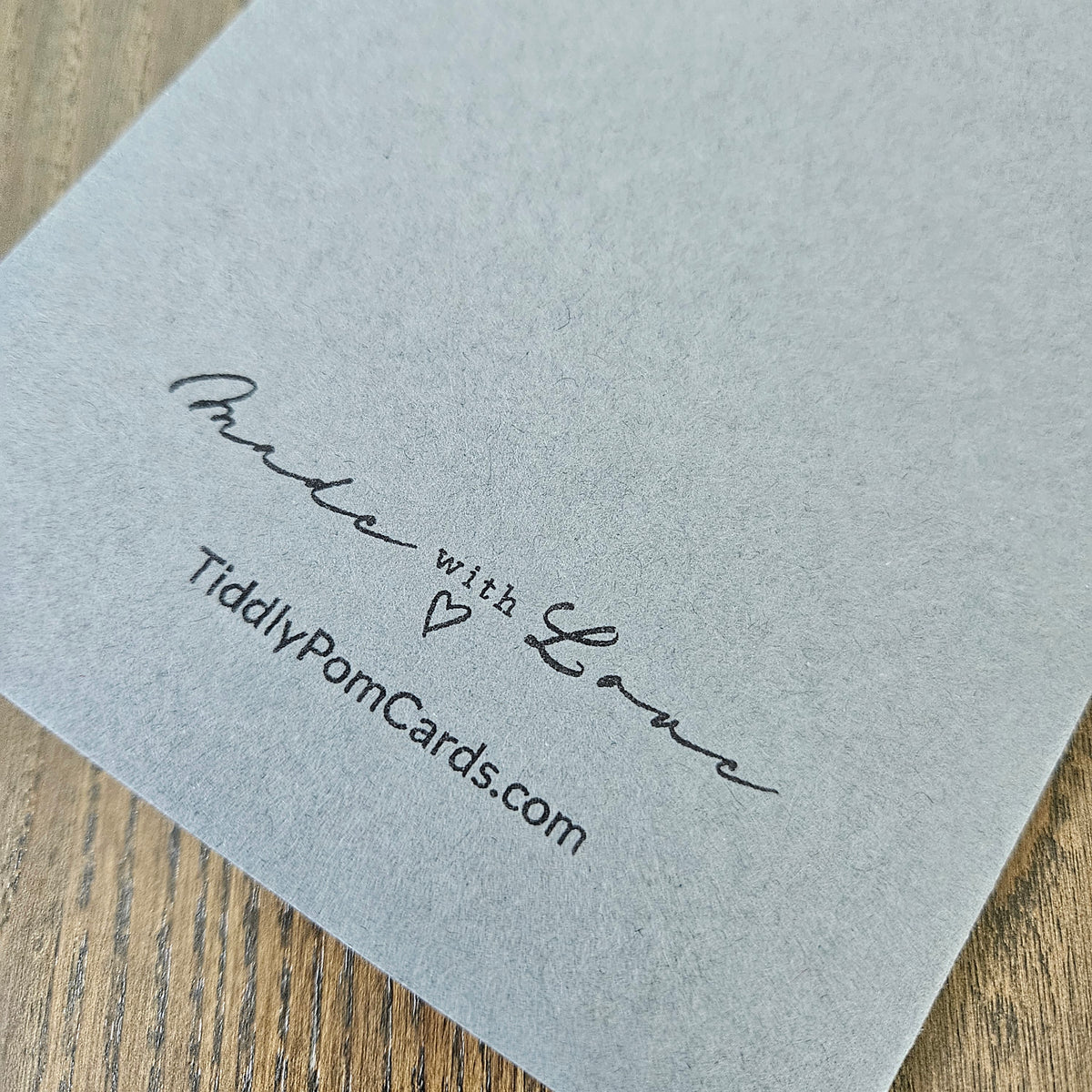 Gray card with 'Made with Love' and 'TiddlyPomCards.com' text on a wooden surface