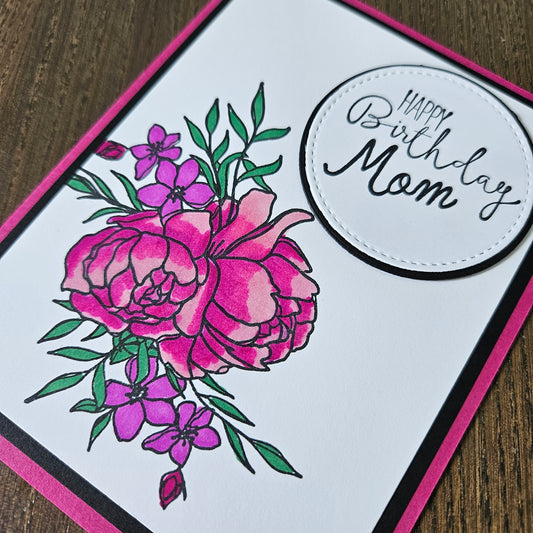 Greeting card with pink flowers and 'Happy Birthday Mom' text on a wooden surface