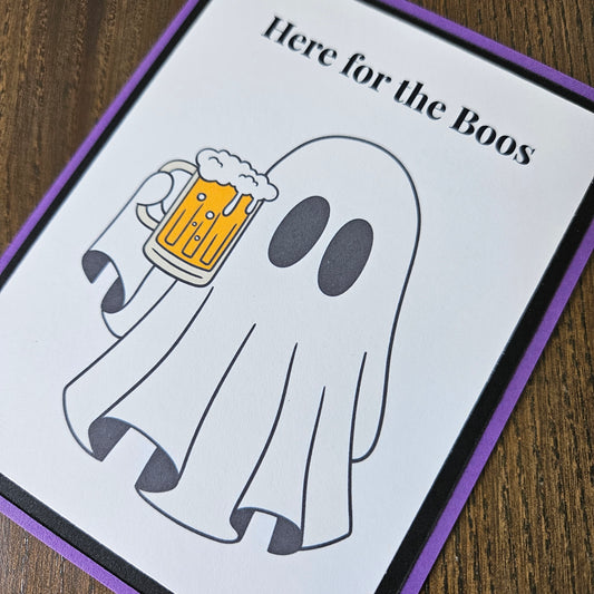 Front of a handmade A2 funny Halloween card featuring a ghost holding a beer mug framed by black and purple borders with text reading Here for the Boos.