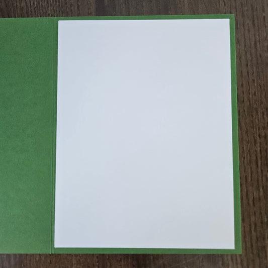 A blank white rectangular card or paper sheet placed on top of a green textured backing, photographed from above on a dark wood surface.