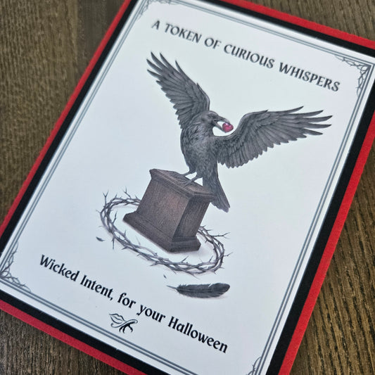 A square Halloween card or print with a white center, red border, black text reading 'A TOKEN OF CURIOUS WHISPS' and 'Wicked Intent, for your Halloween,' plus an illustration of a raven perched on a pedestal with a crown of thorns and a feather.