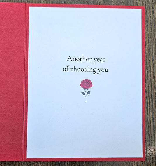 Inside of red husband birthday card reading Another year of choosing you, with a small red rose illustration.