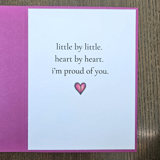 Inside of magenta card reading little by little, heart by heart, I'm proud of you, with a small pink stitched-heart illustration.