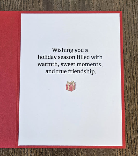 Printed inside of the red Christmas card reading Wishing you a holiday season filled with warmth, sweet moments, and true friendship, with a small present below.