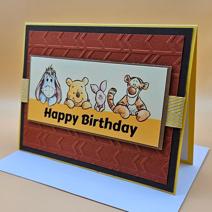 Birthday card with cartoon characters and 'Happy Birthday' text on a brown and yellow background.