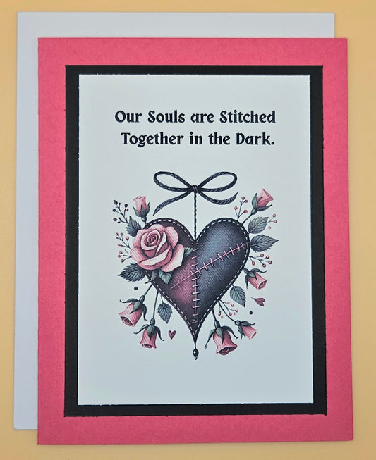 Handmade Gothic love card with stitched dark heart and rose accents on dark background. Text reads Our souls are stitched together in the dark.