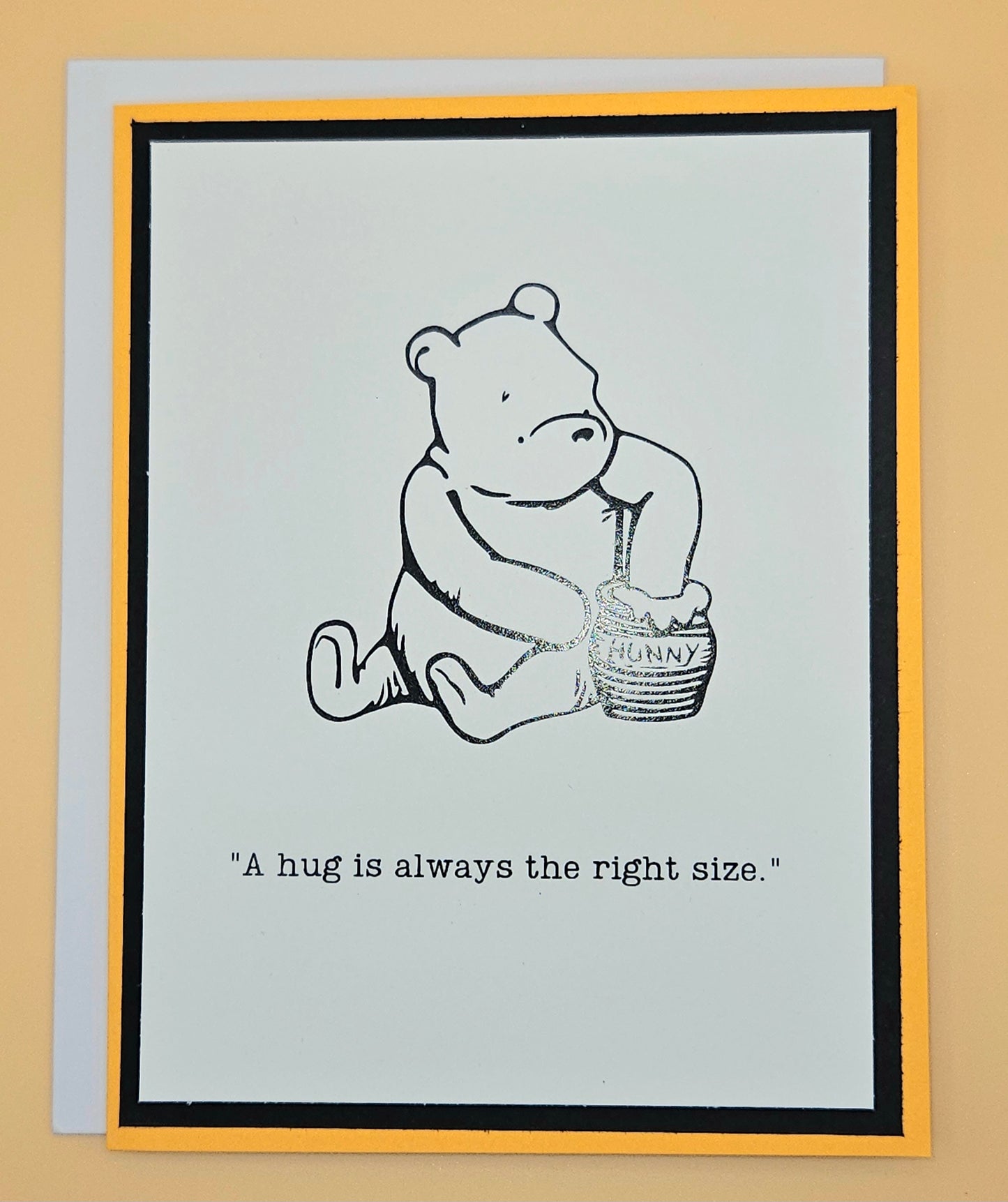 Card with a bear holding a honey pot and text 'A hug is always the right size.' on a beige background