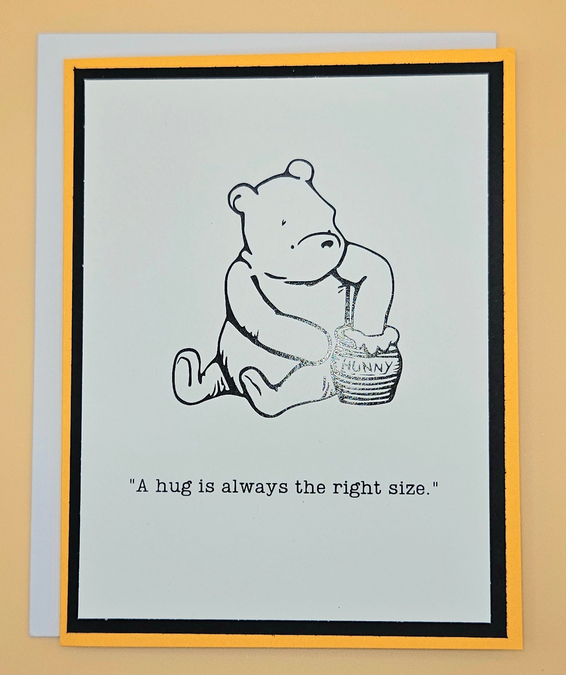 Card with a bear holding a honey pot and text 'A hug is always the right size.' on a beige background