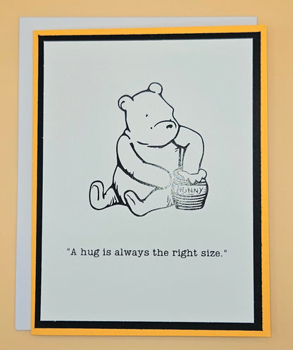 Card with a bear holding a honey pot and text 'A hug is always the right size.' on a beige background