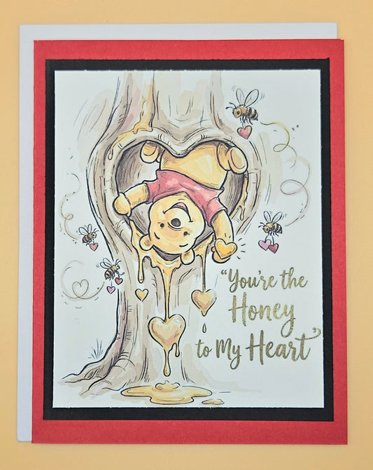 Card with cartoon character in a heart shape and 'You're the Honey to My Heart' text on a beige background.