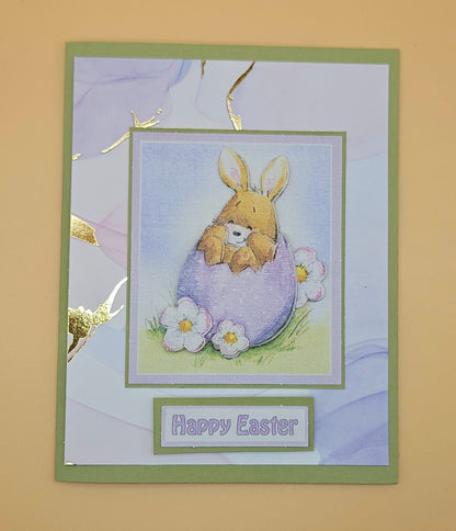 Easter card with a bunny holding a teddy bear in an egg, surrounded by flowers on a beige background.