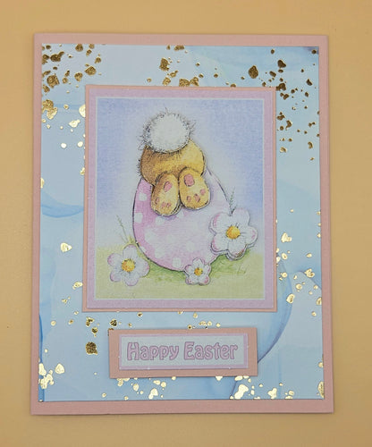 Easter card with a bunny in an egg, flowers, and 'Happy Easter' text on a blue background.