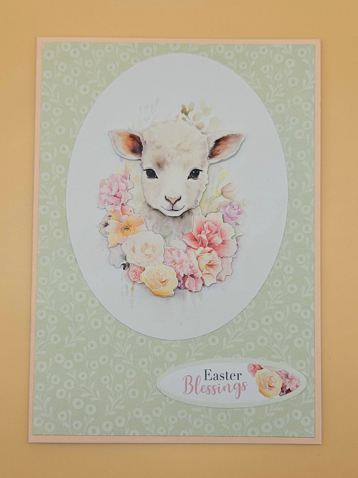 Card with a lamb illustration and floral wreath on a light green background with 'Easter Blessings' text.