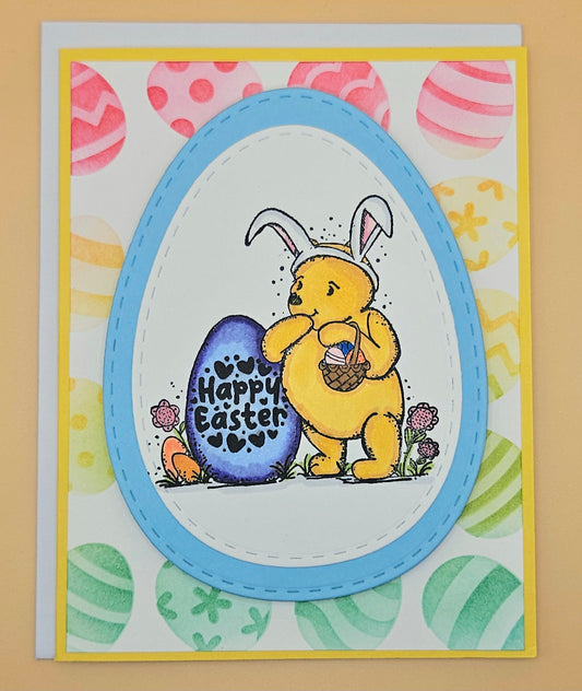 Easter card with a bear wearing bunny ears holding a blue egg with 'Happy Easter' text, surrounded by colorful Easter eggs and patterns.