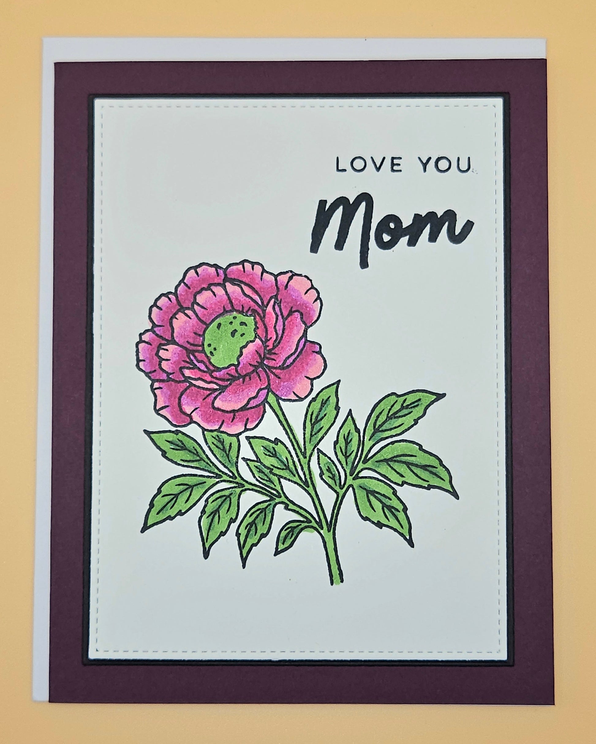 Greeting card with pink flower illustration and 'Love You Mom' text on a beige background