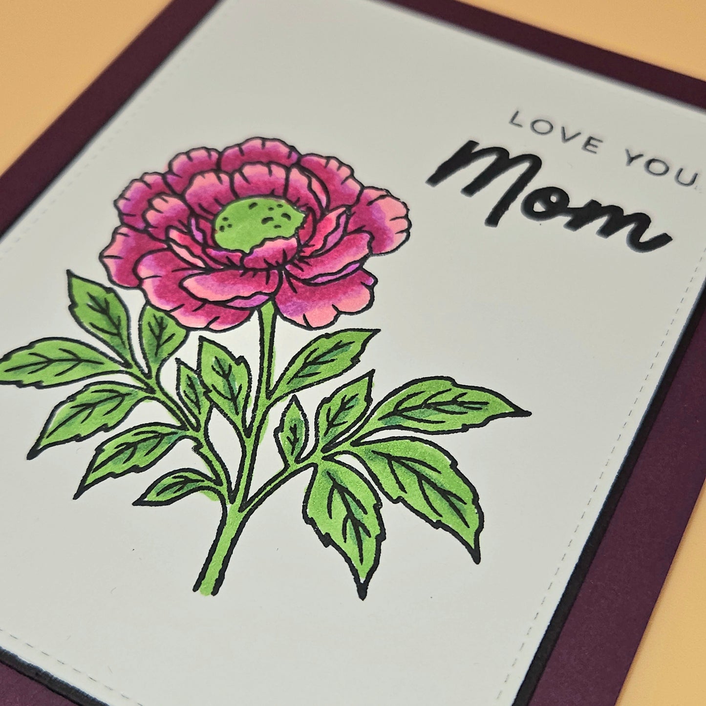 Card with a pink flower illustration and 'Love You Mom' text on a beige background