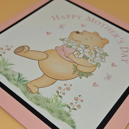 Mother's Day card with a teddy bear holding flowers on a pink border.