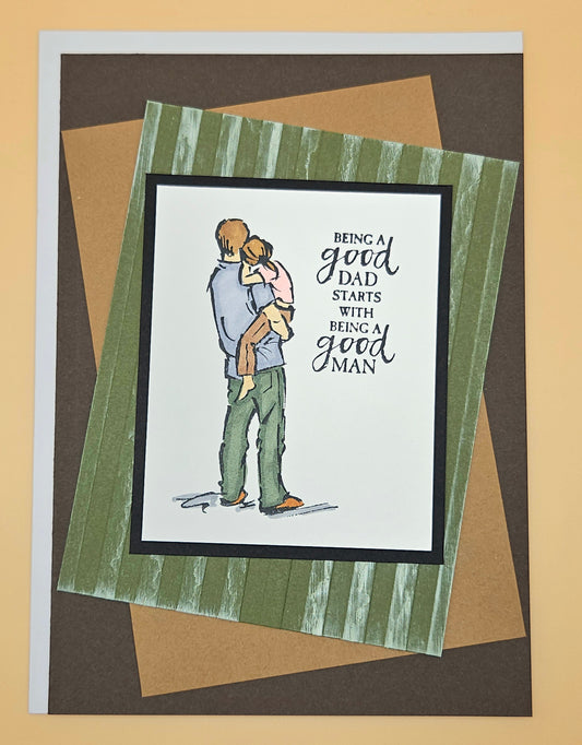 Card with illustration of a father holding a child and text 'Being a good dad starts with being a good man' on a striped background.