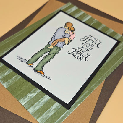 Card with illustration of a man lifting a woman and text 'Being a good dad starts with being a good man' on a striped background.