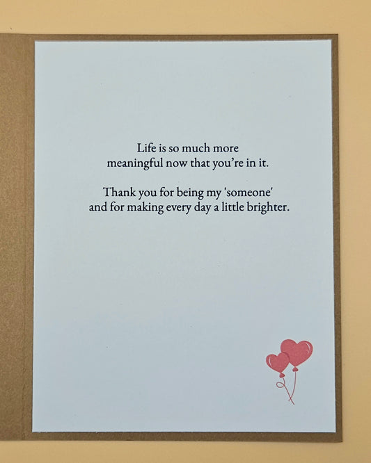 Card with a message and heart-shaped balloons on a light blue background, framed in brown.