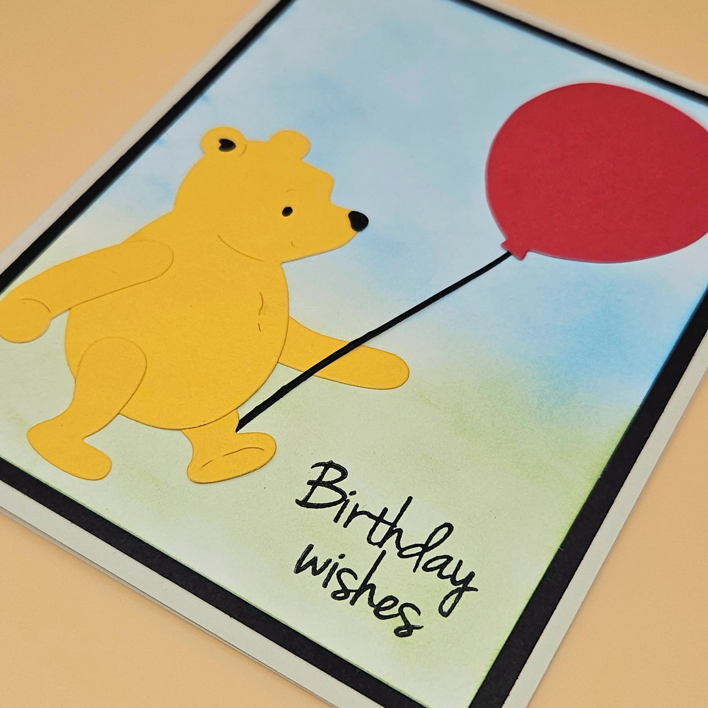Cartoon bear holding a red balloon with 'Birthday wishes' text on a colorful background