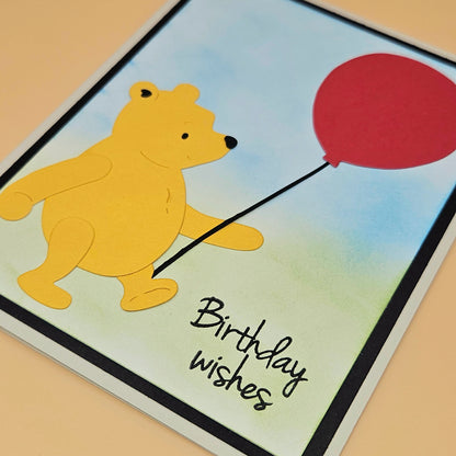 Cartoon bear holding a red balloon with 'Birthday wishes' text on a colorful background