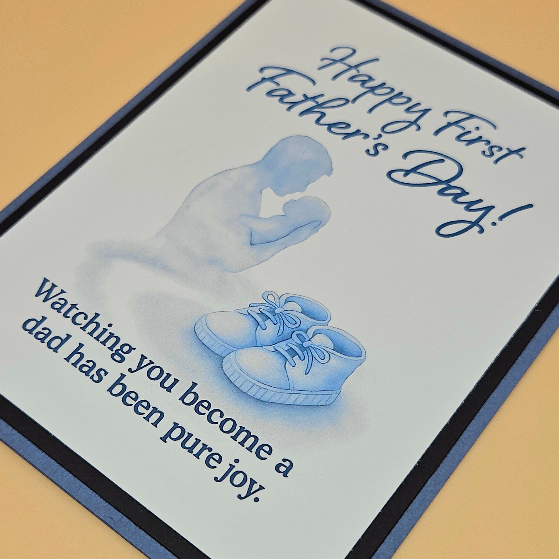 Father's Day card with silhouette of a father and baby shoes, text 'Happy First Father's Day!'.