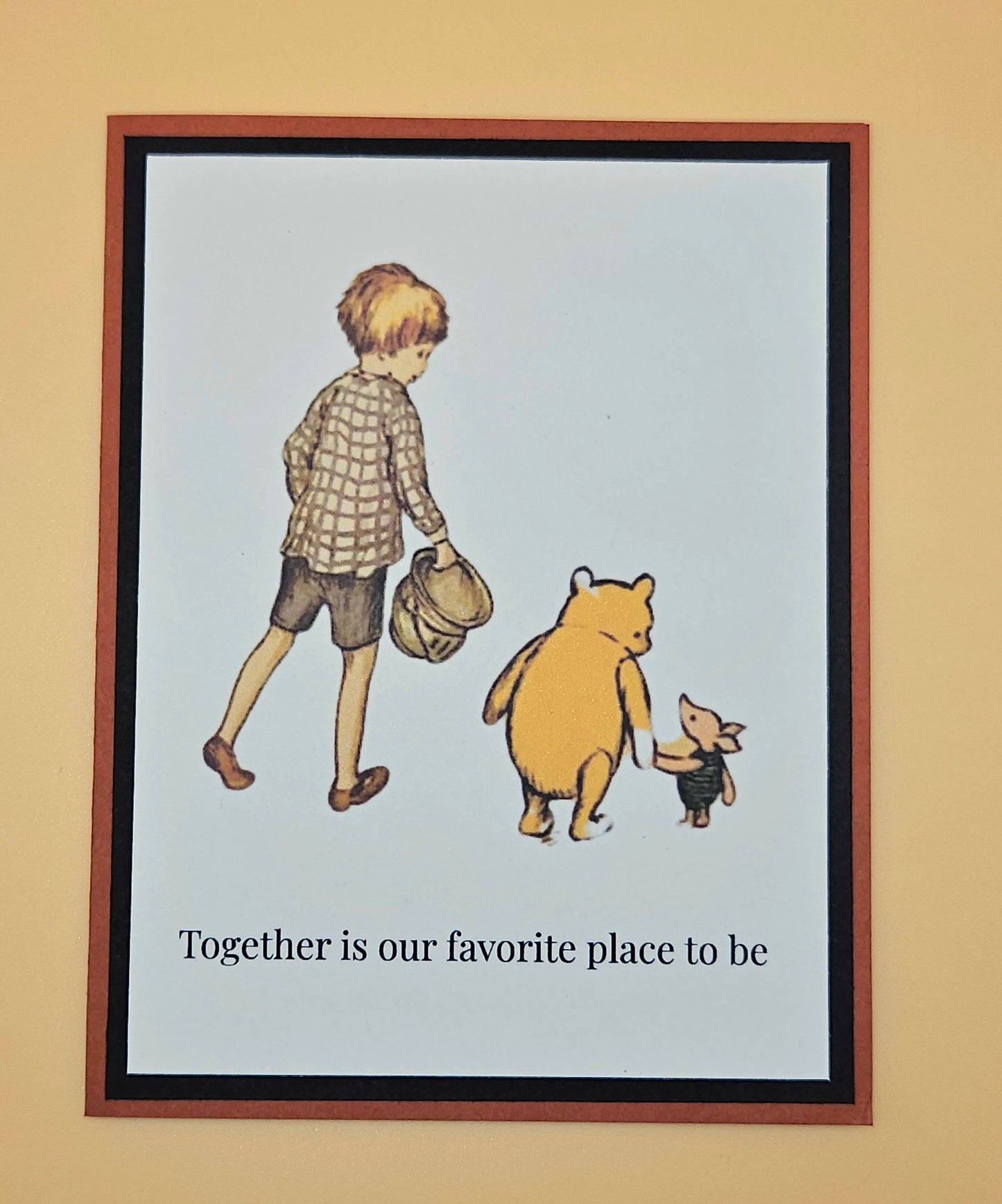 Framed illustration of a boy, bear, and piglet with text 'Together is our favorite place to be' on a beige wall.