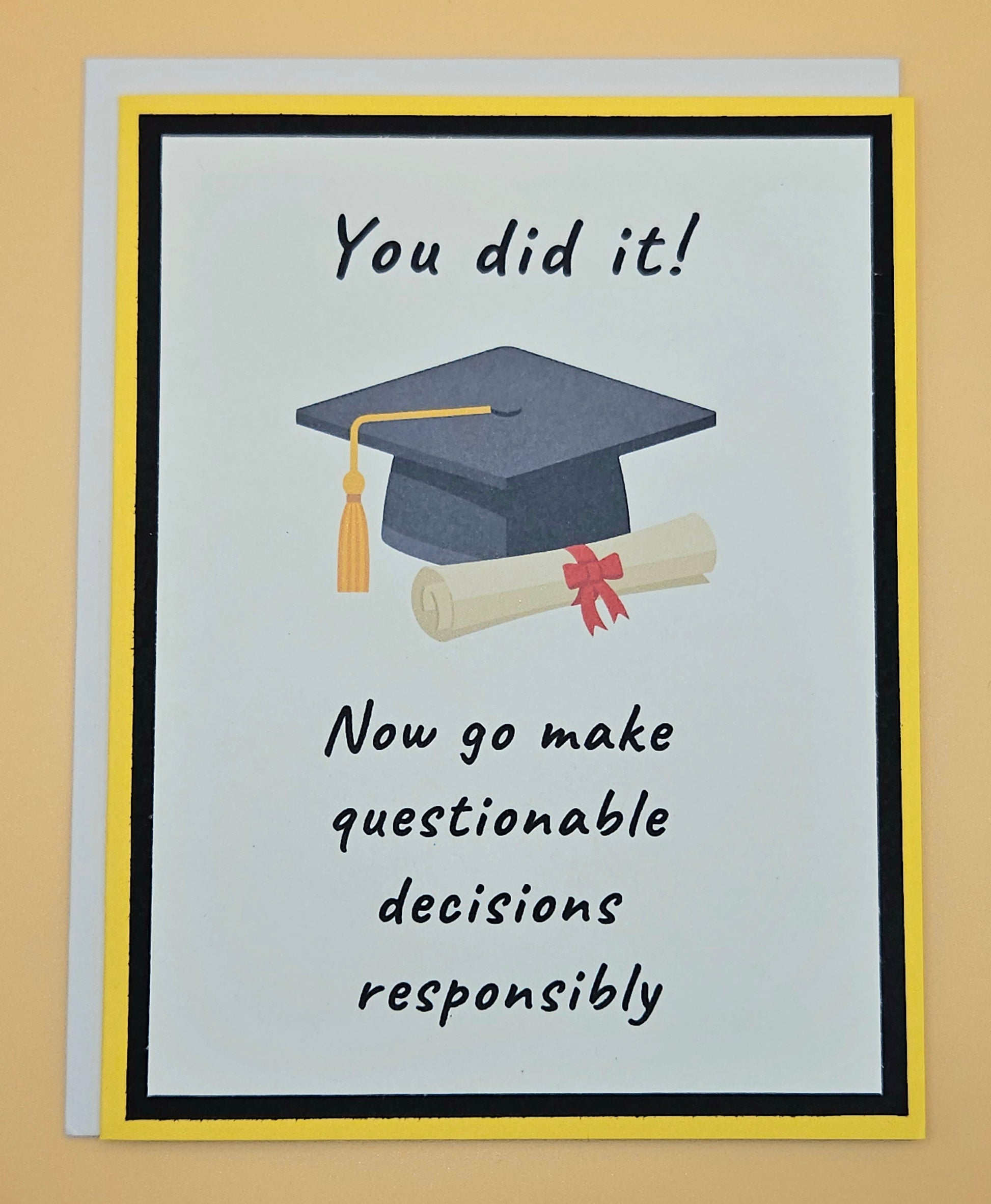 Handmade funny graduation card with mortarboard and diploma on white panel with black and yellow border. Front reads You Did It Now Go Make Questionable Decisions Responsibly.