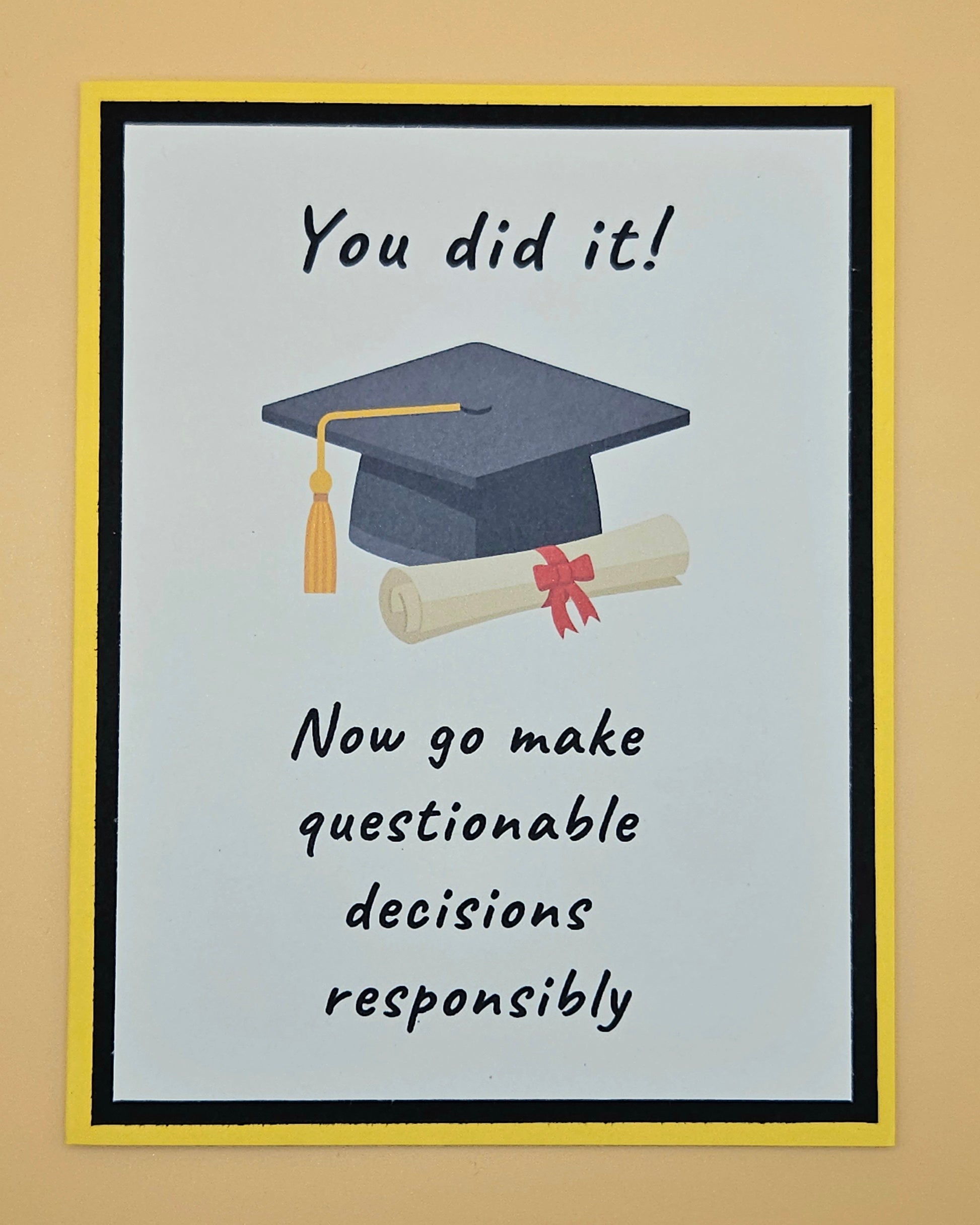 Handmade funny graduation card with mortarboard and diploma on white panel with black and yellow border. Front reads You Did It Now Go Make Questionable Decisions Responsibly.