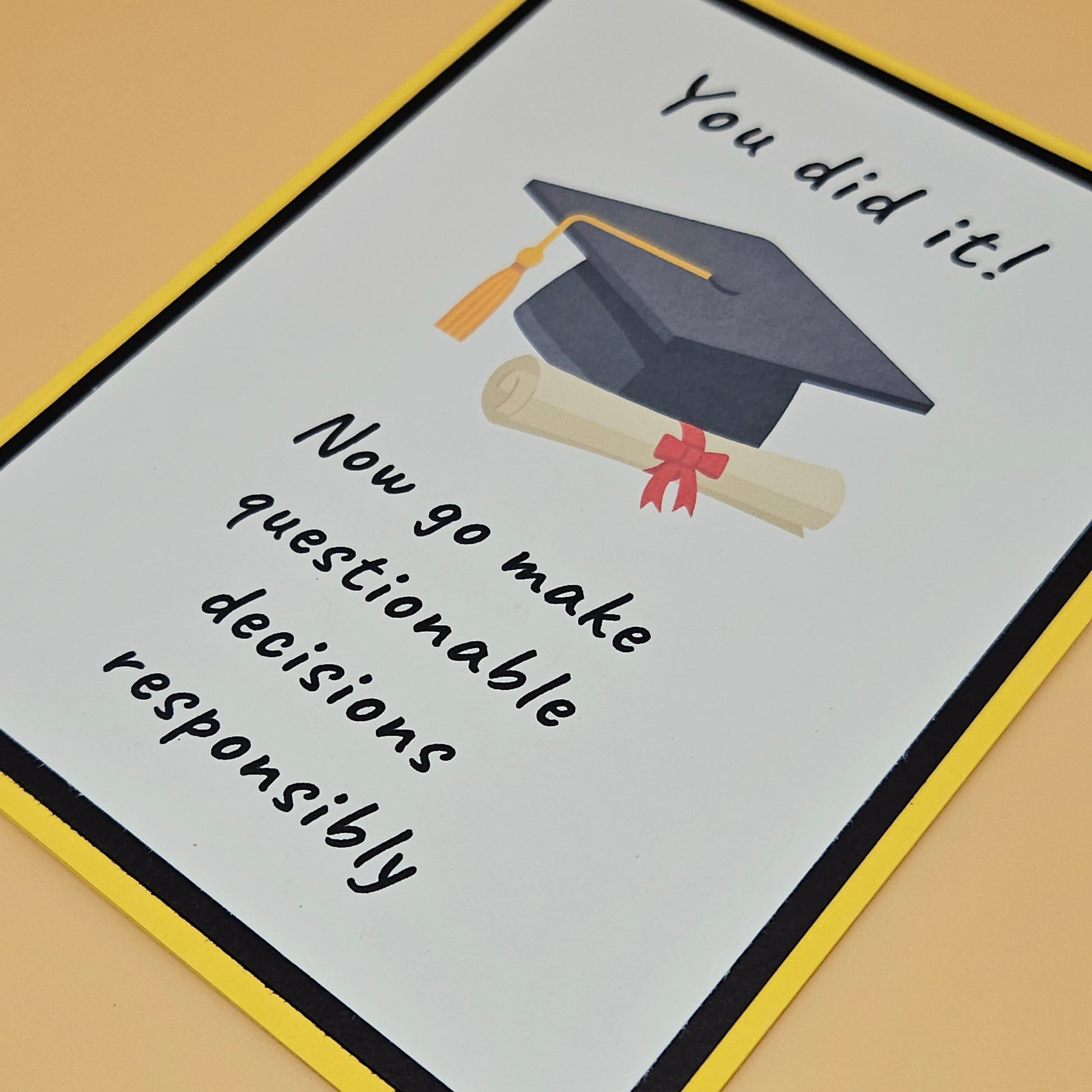 Graduation-themed card with cap, diploma, and humorous text on a beige background. Tiddly Pom Cards