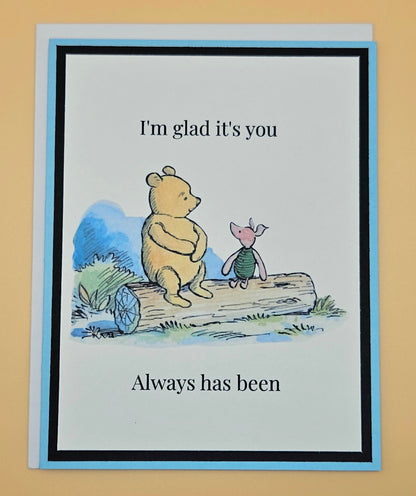 Handmade Winnie the Pooh and Piglet friendship card with Pooh and Piglet sitting on a log in watercolor style on white inner panel with black and sky blue border. Text reads I'm glad it's you always has been.