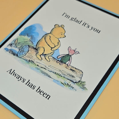 Handmade Winnie the Pooh and Piglet friendship card with Pooh and Piglet sitting on a log in watercolor style on white inner panel with black and sky blue border. Text reads I'm glad it's you always has been.