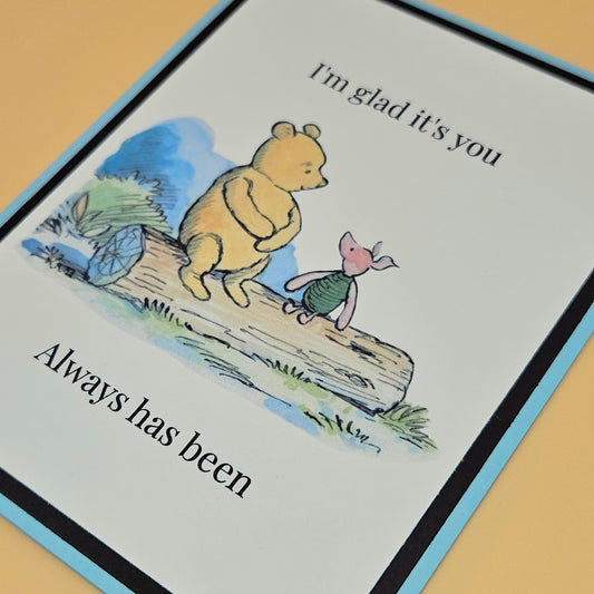 Handmade Winnie the Pooh and Piglet friendship card with Pooh and Piglet sitting on a log in watercolor style on white inner panel with black and sky blue border. Text reads I'm glad it's you always has been.