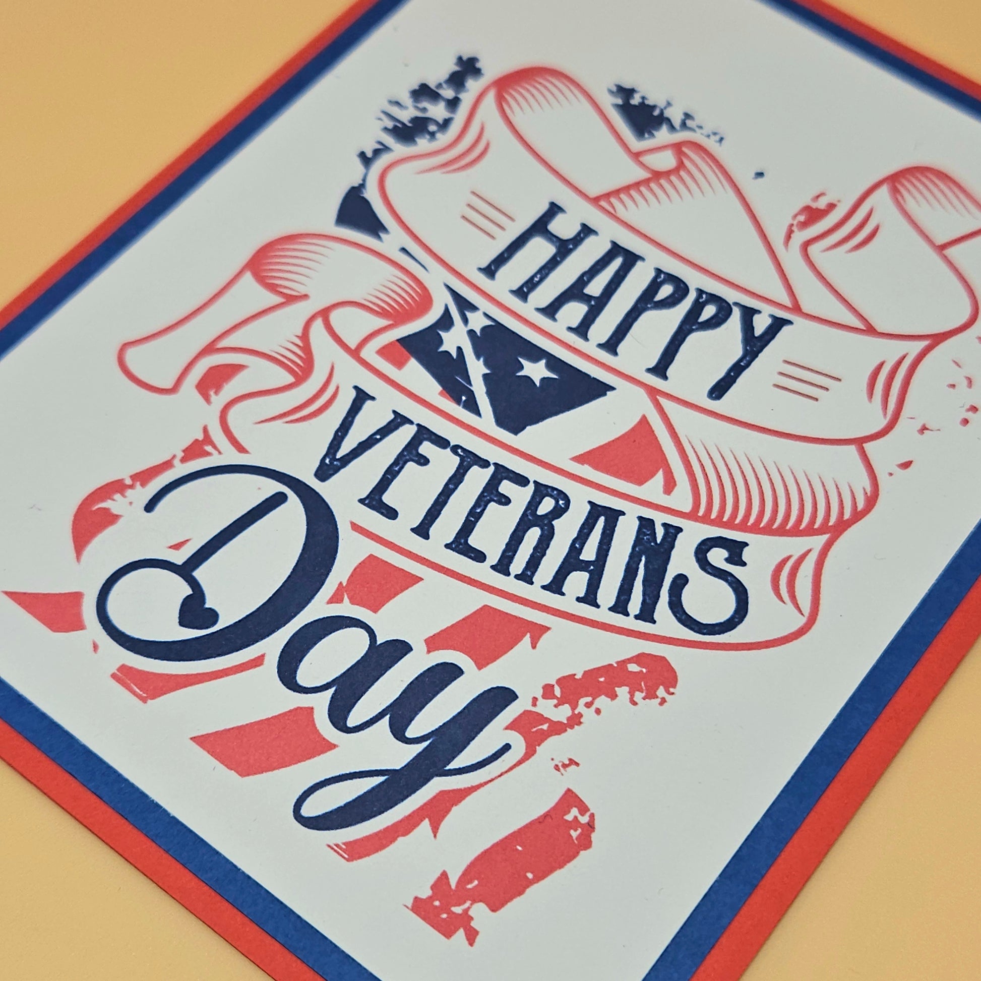 Handmade Veterans Day card with bold patriotic ribbon banner and stars and stripes design on white inner panel with black navy and red borders. Text reads Happy Veterans Day. TiddlyPomCards.com