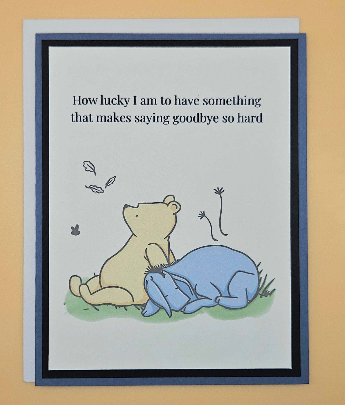 Handmade Winnie the Pooh goodbye card with Pooh comforting Eeyore beneath falling autumn leaves on white inner panel with black and slate blue border. Text reads How lucky I am to have something that makes saying goodbye so hard.