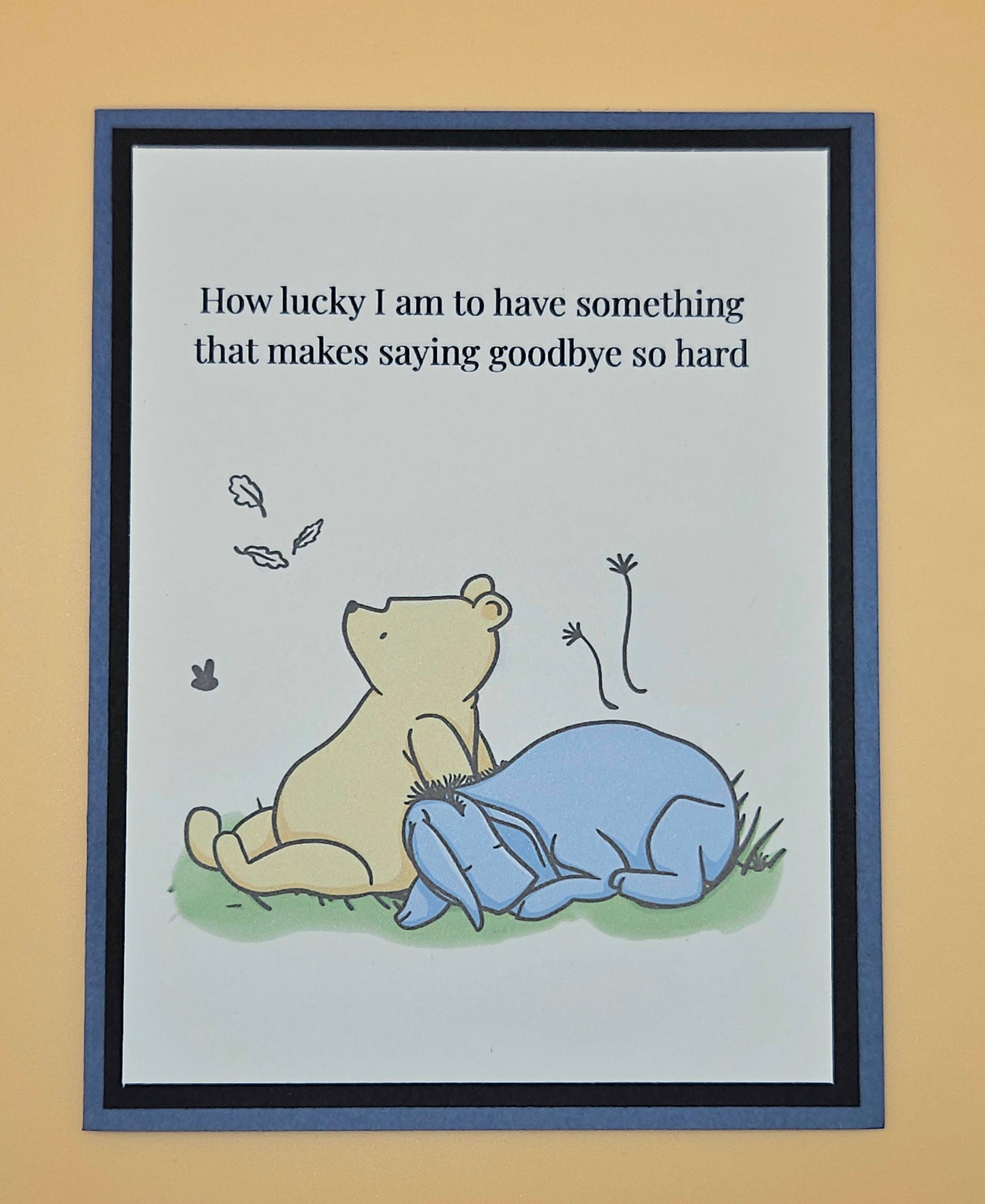 Handmade Winnie the Pooh goodbye card with Pooh comforting Eeyore beneath falling autumn leaves on white inner panel with black and slate blue border. Text reads How lucky I am to have something that makes saying goodbye so hard.
