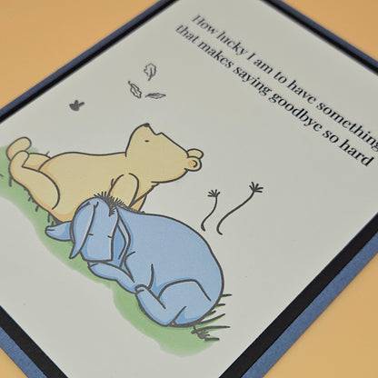 Handmade Winnie the Pooh goodbye card with Pooh comforting Eeyore beneath falling autumn leaves on white inner panel with black and slate blue border. Text reads How lucky I am to have something that makes saying goodbye so hard.