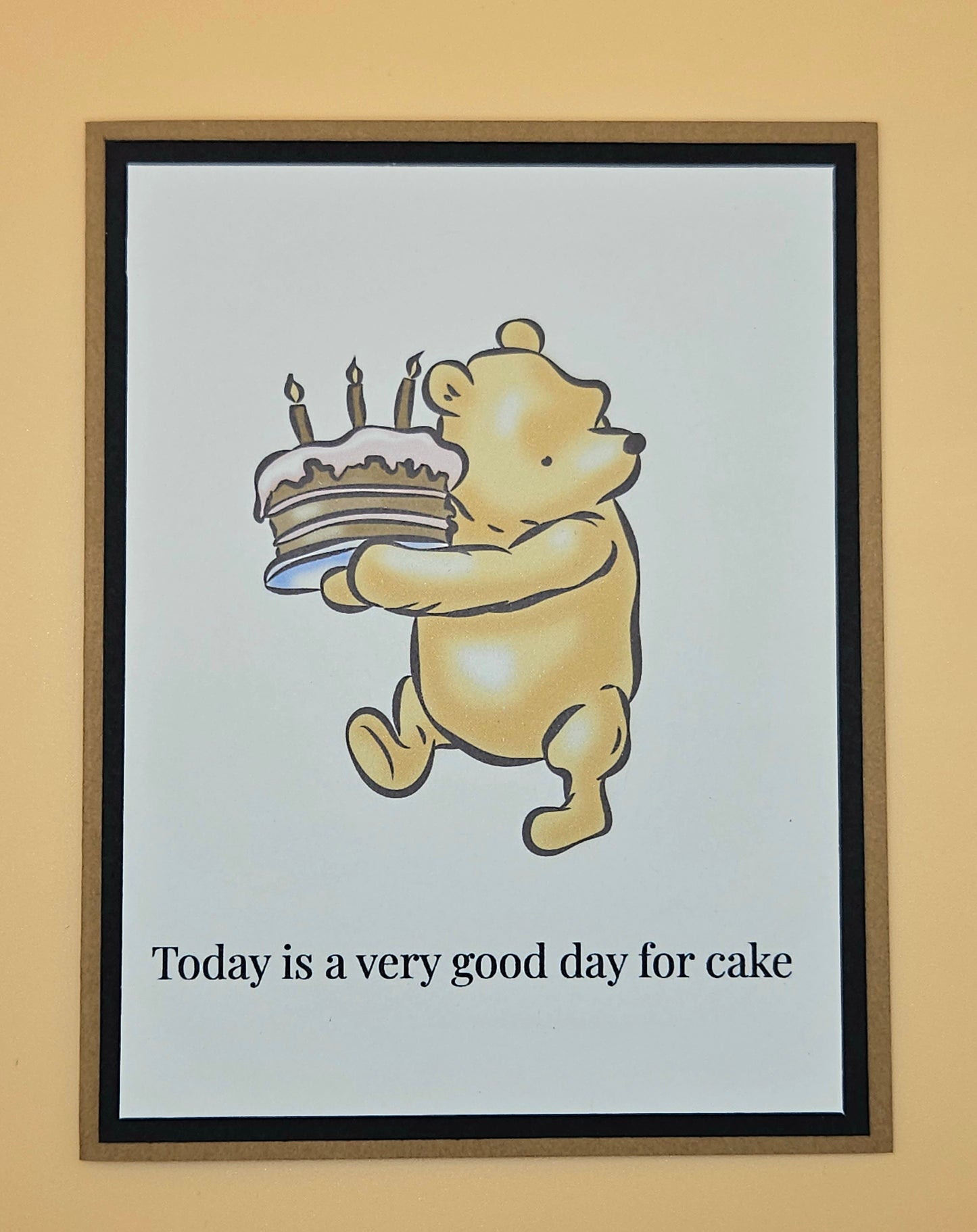 Handmade Winnie the Pooh birthday card with Pooh carrying a birthday cake with lit candles on white inner panel with black and tan border. Text reads Today is a very good day for cake.