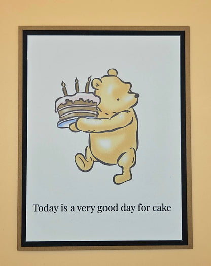 Handmade Winnie the Pooh birthday card with Pooh carrying a birthday cake with lit candles on white inner panel with black and tan border. Text reads Today is a very good day for cake.