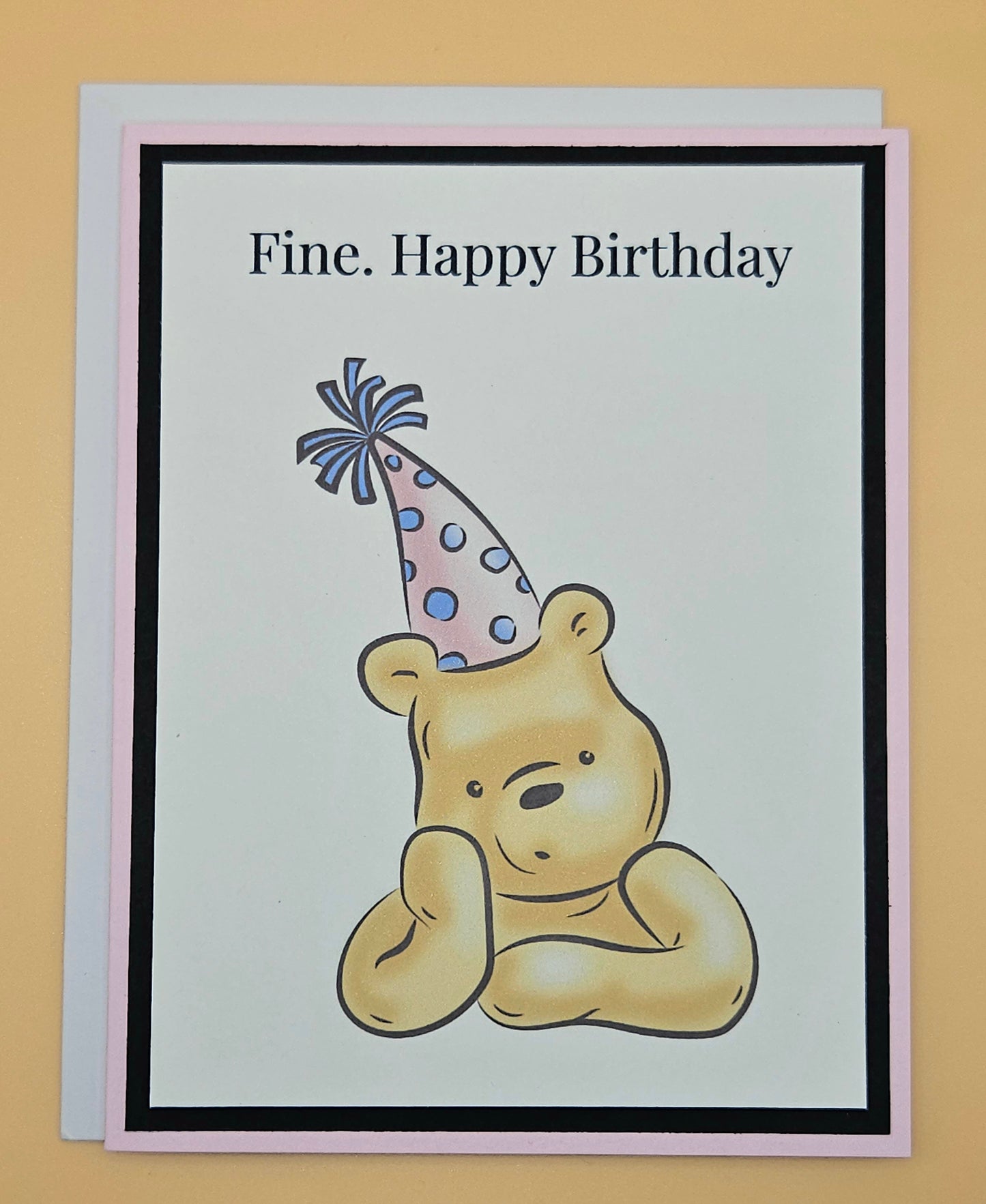 Handmade funny Winnie the Pooh birthday card with grumpy Pooh sitting arms crossed wearing a pink polka dot party hat on white inner panel with black and pink border. Text reads Fine Happy Birthday.