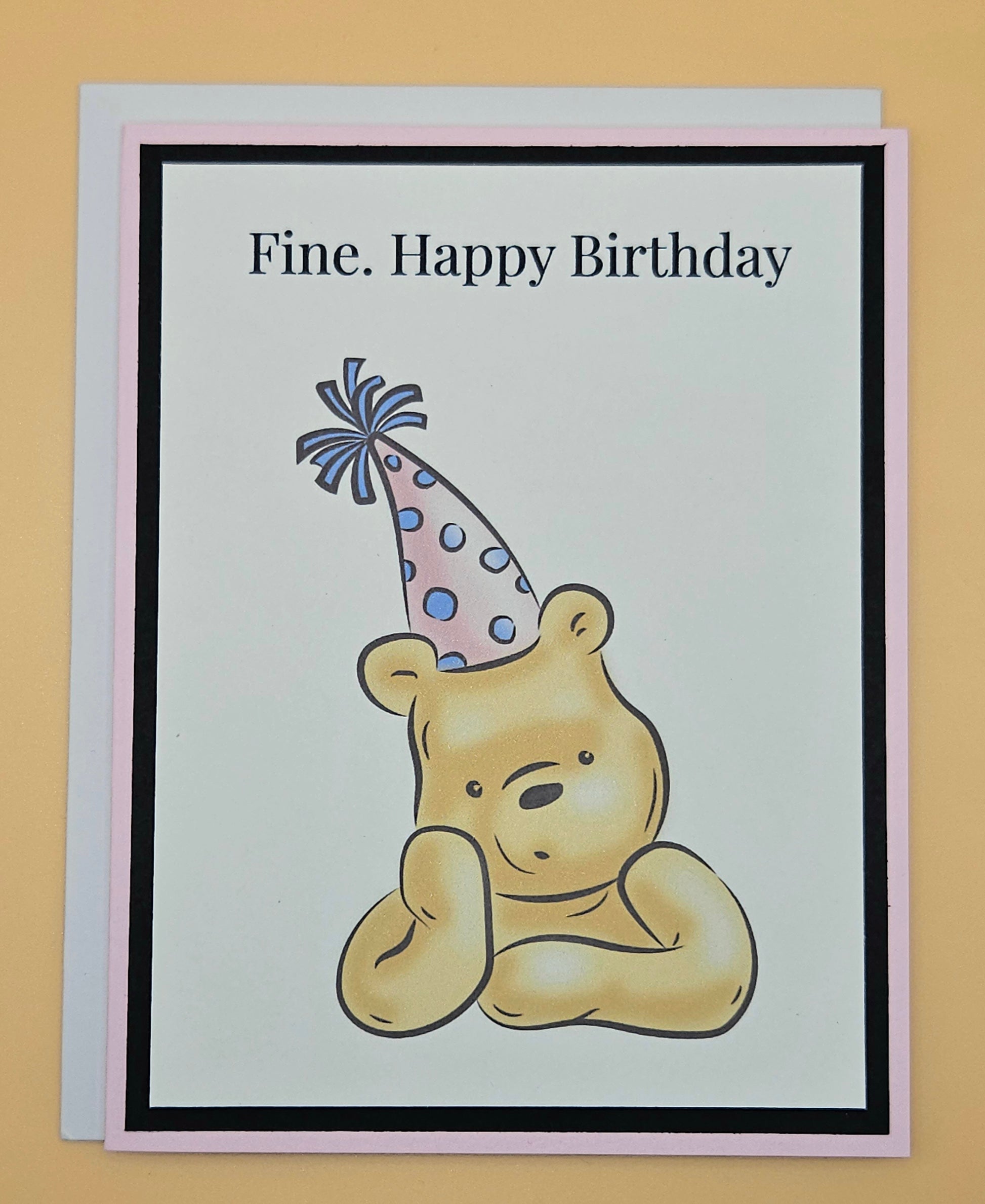 Handmade funny Winnie the Pooh birthday card with grumpy Pooh sitting arms crossed wearing a pink polka dot party hat on white inner panel with black and pink border. Text reads Fine Happy Birthday.