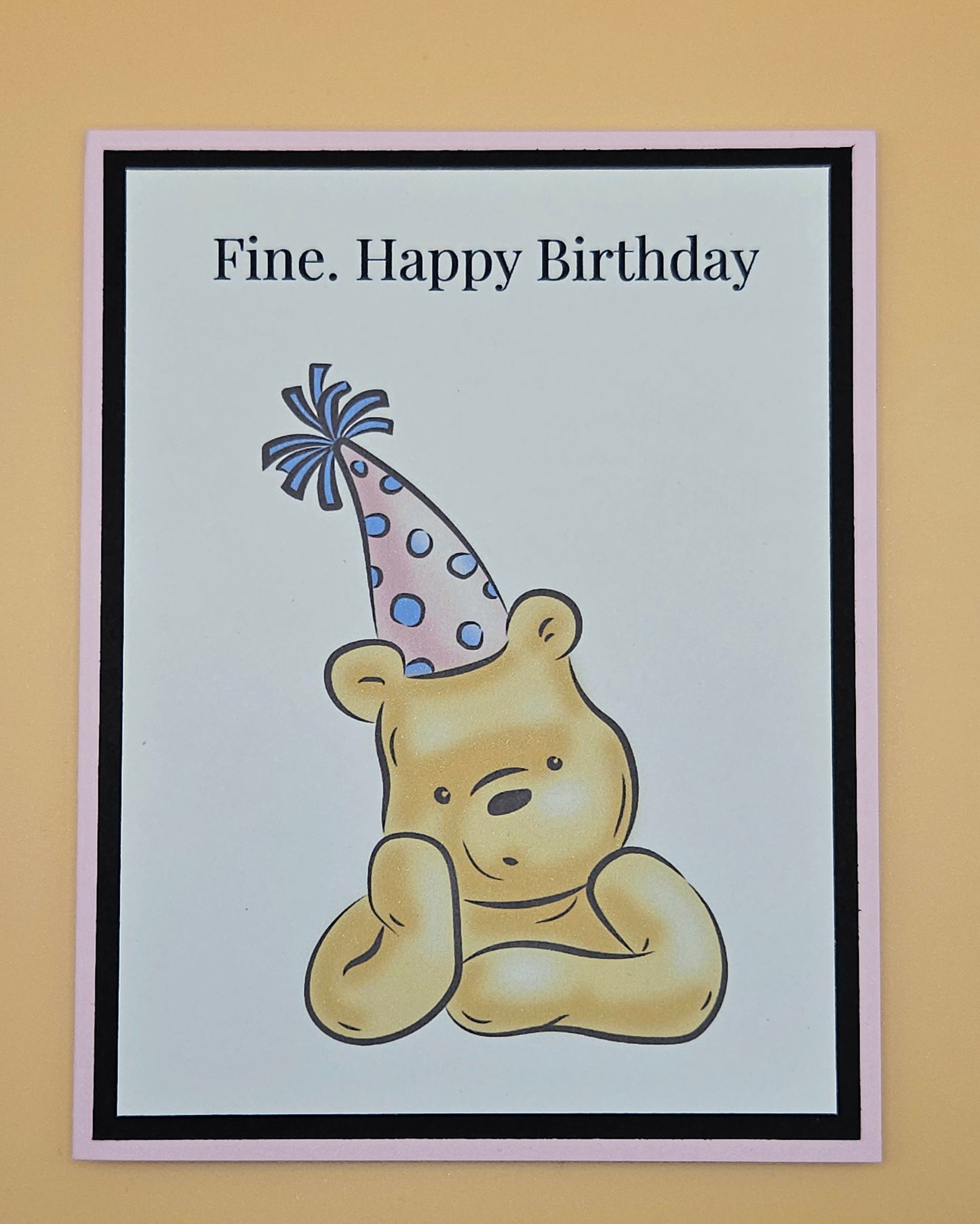 Handmade funny Winnie the Pooh birthday card with grumpy Pooh sitting arms crossed wearing a pink polka dot party hat on white inner panel with black and pink border. Text reads Fine Happy Birthday.